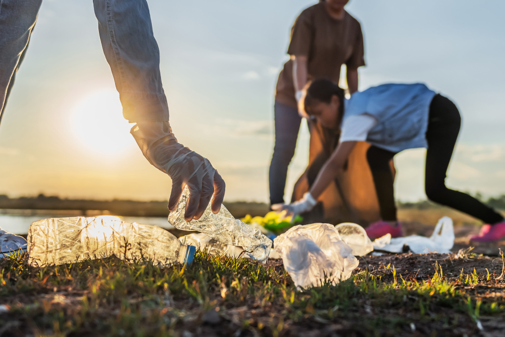 people-volunteer-keeping-garbage-plastic-bottle-into-black-bag-at-park-near-river-in-sunset